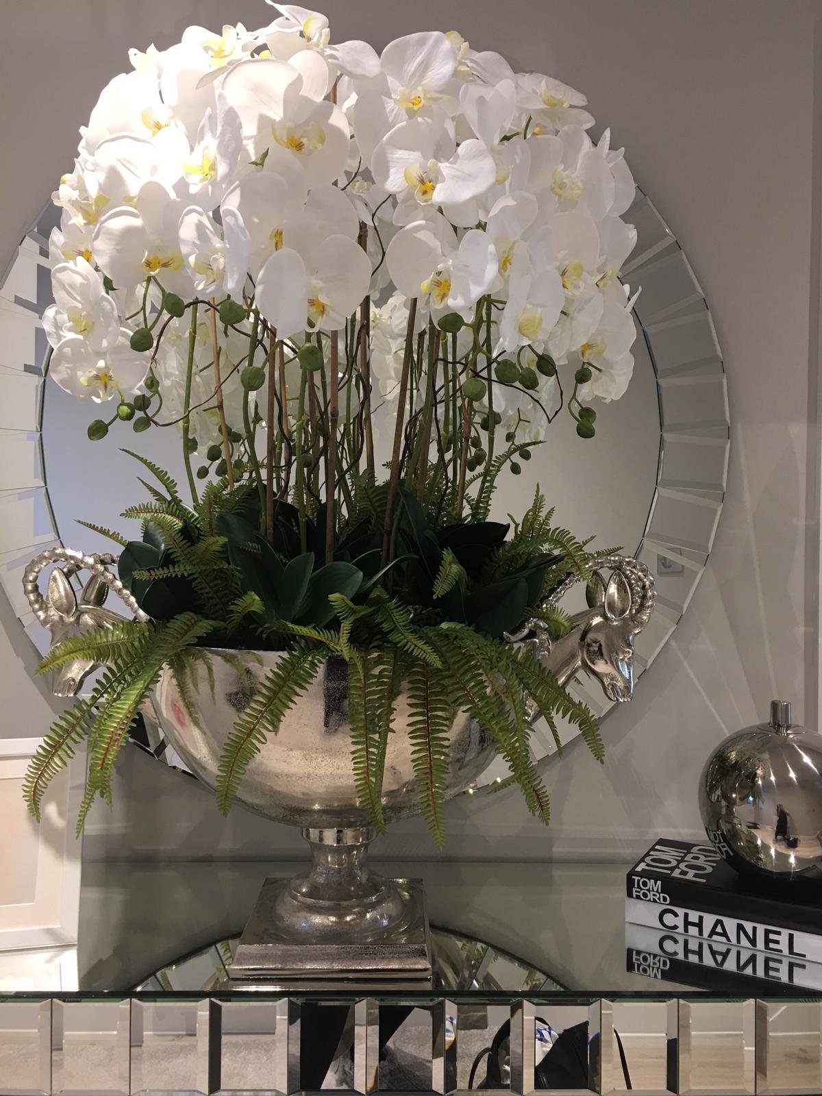 Faux orchids in a rams head urn on a console, the kind of piece that suits a hotel corridor
